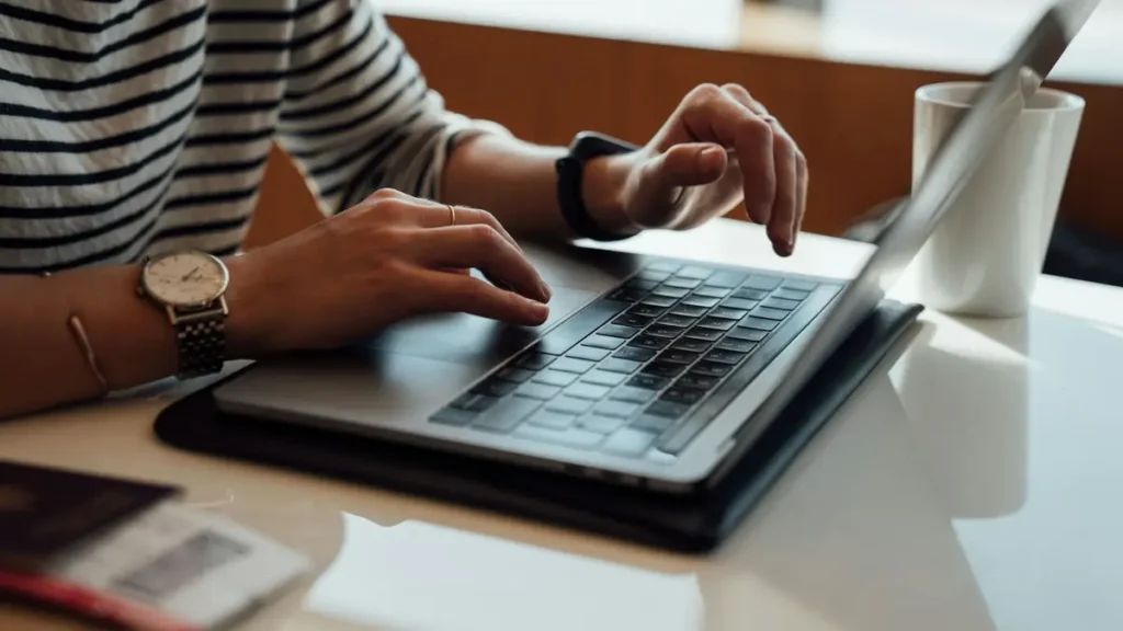 Mains qui tapent sur un ordinateur portable à côté d'une tasse