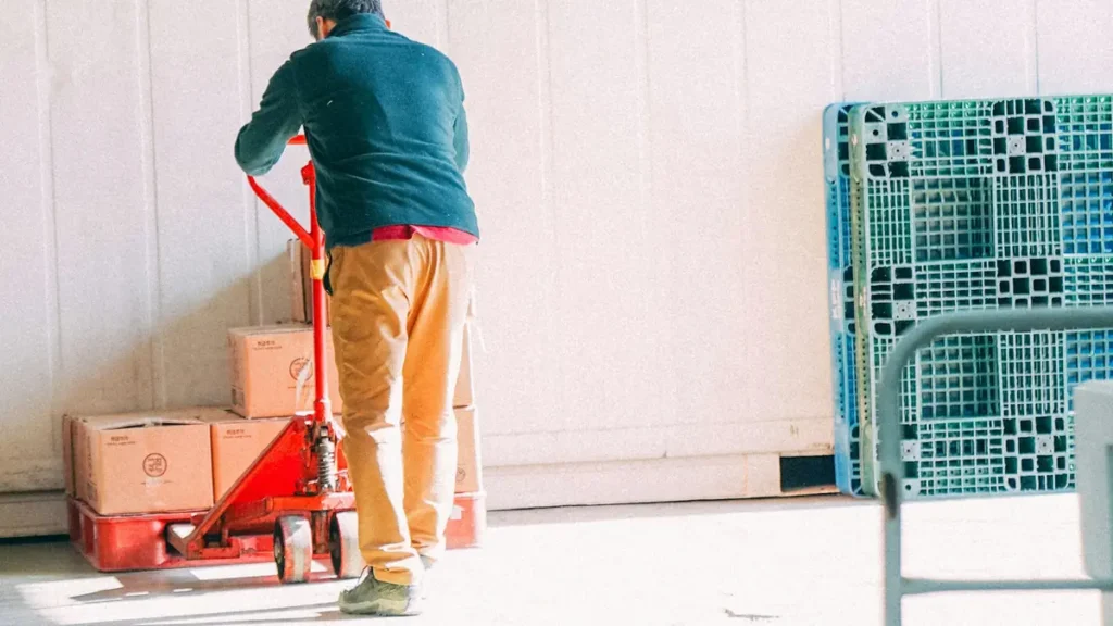 Homme qui tire un transpalette chargé de cartons