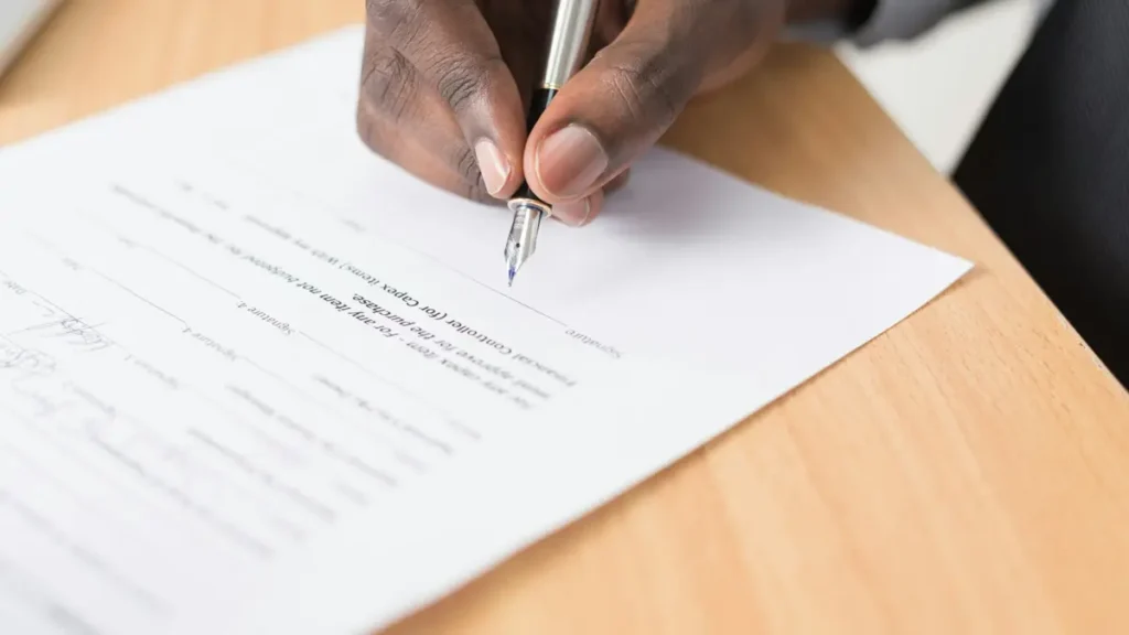 Main qui écrit sur une feuille posée sur un bureau