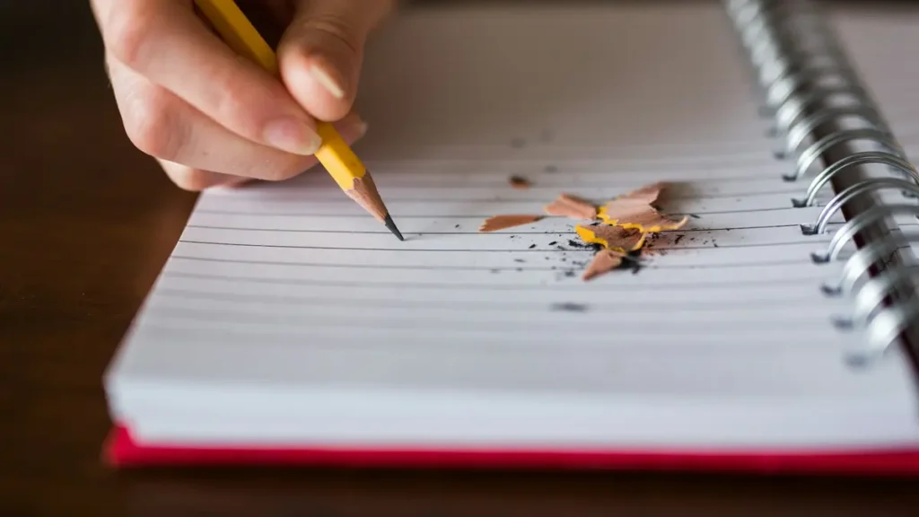 Main qui écrit au crayon dans un carnet à spirale