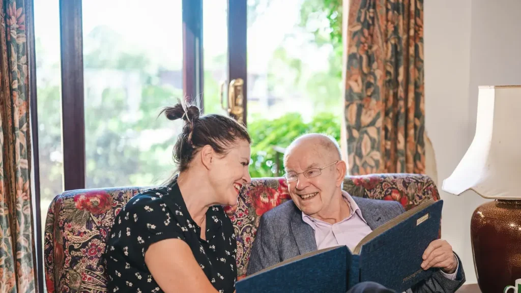 Intervenante souriante qui regarde un album avec un homme âgé