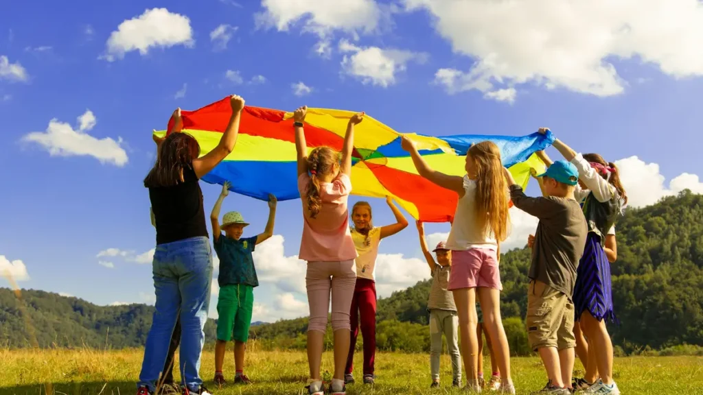Enfants et animateurs qui jouent avec un parachute coloré dans un pré