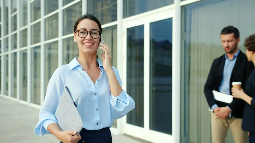 Assistante souriante qui téléphone devant un immeuble de bureaux