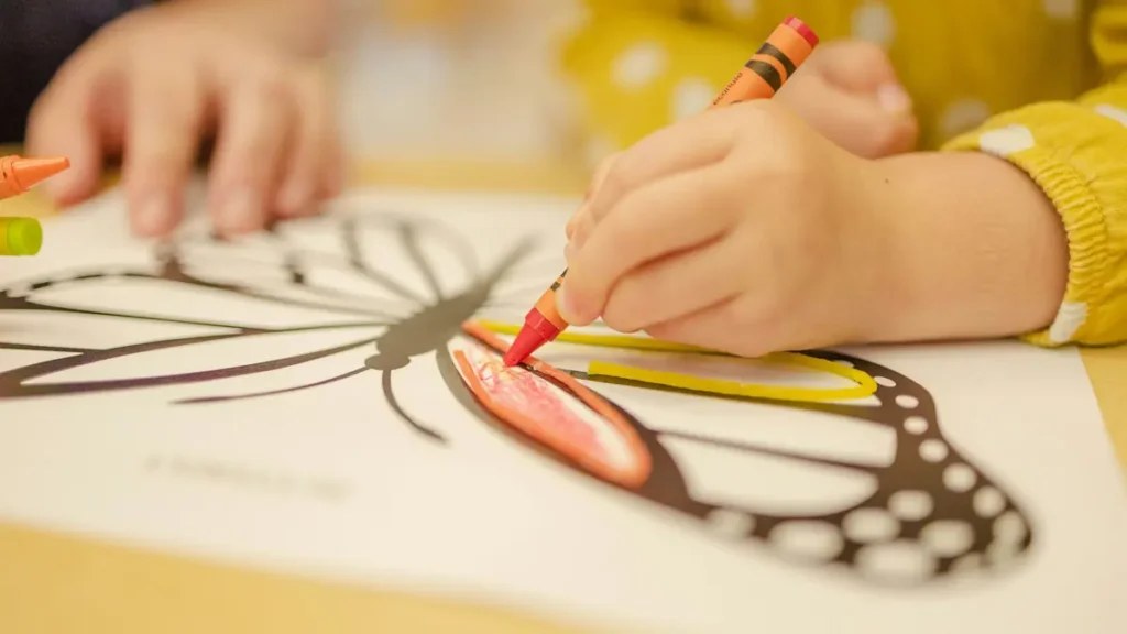 Enfant qui colorie un papillon avec un crayon rouge