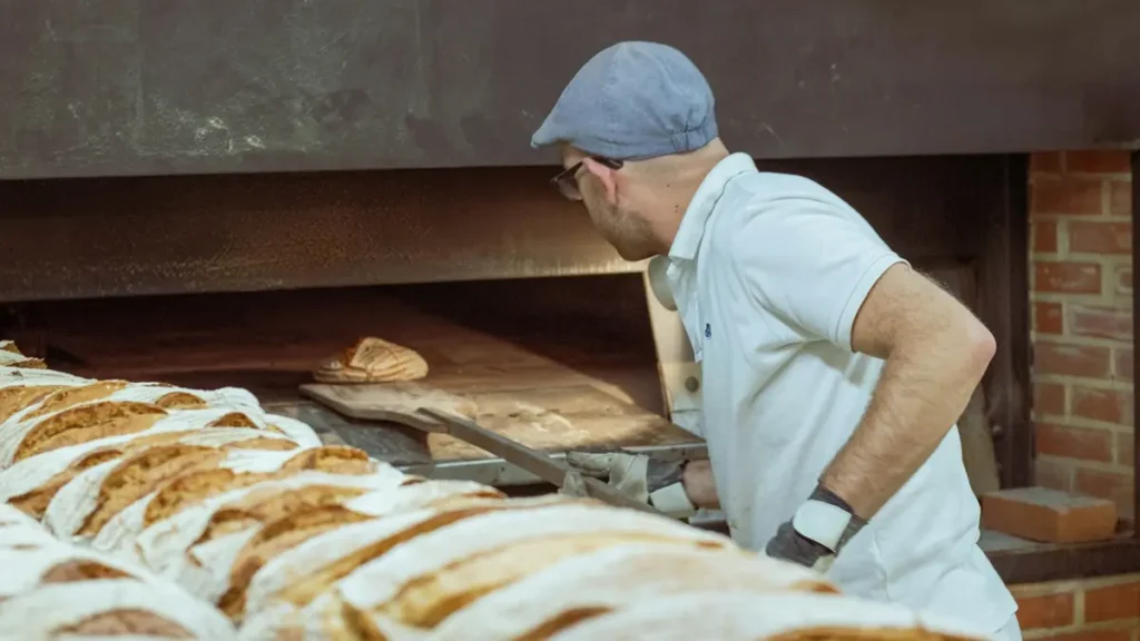 Boulanger qui enfourne des pains dans un four à bois