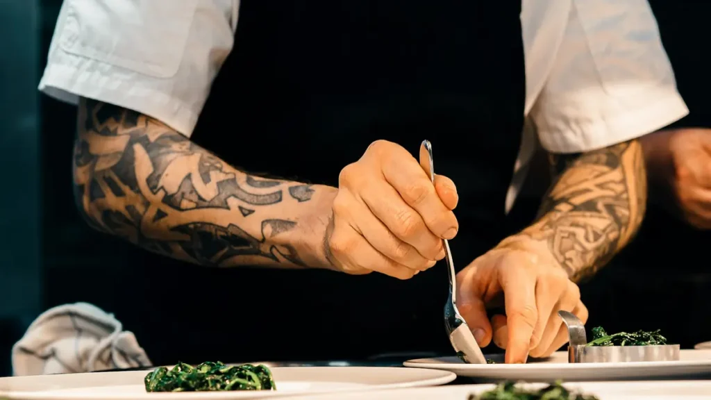 Chef tatoué qui dresse une assiette à la pince