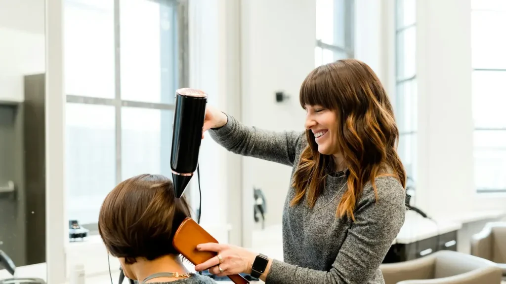 Coiffeuse souriante qui sèche les cheveux d'une cliente