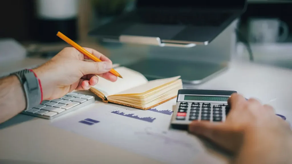 Mains qui utilisent une calculatrice et un carnet à côté d'un clavier
