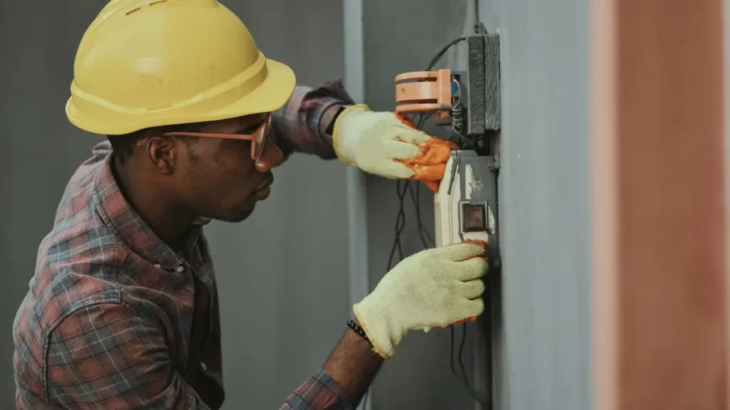 Électricien casqué qui intervient sur une installation murale