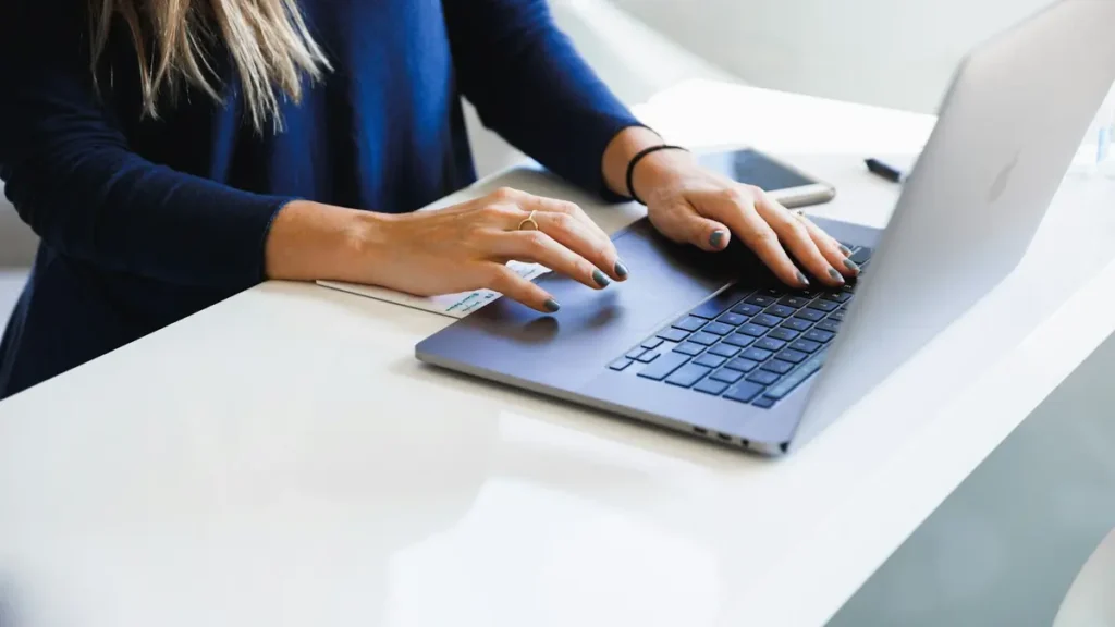 Mains qui tapent sur un ordinateur portable posé sur un bureau blanc