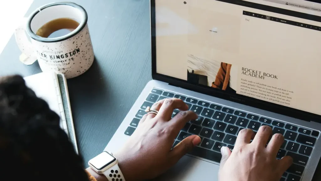 Mains qui tapent sur un ordinateur portable à côté d'une tasse