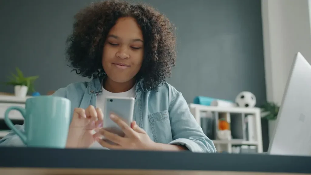 Lycéenne souriante qui regarde son téléphone à un bureau