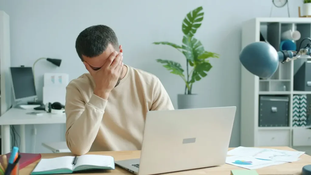 Homme découragé, la main sur le front devant son ordinateur