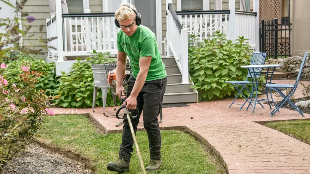 Jardinier qui taille les bordures d'une pelouse avec une débroussailleuse