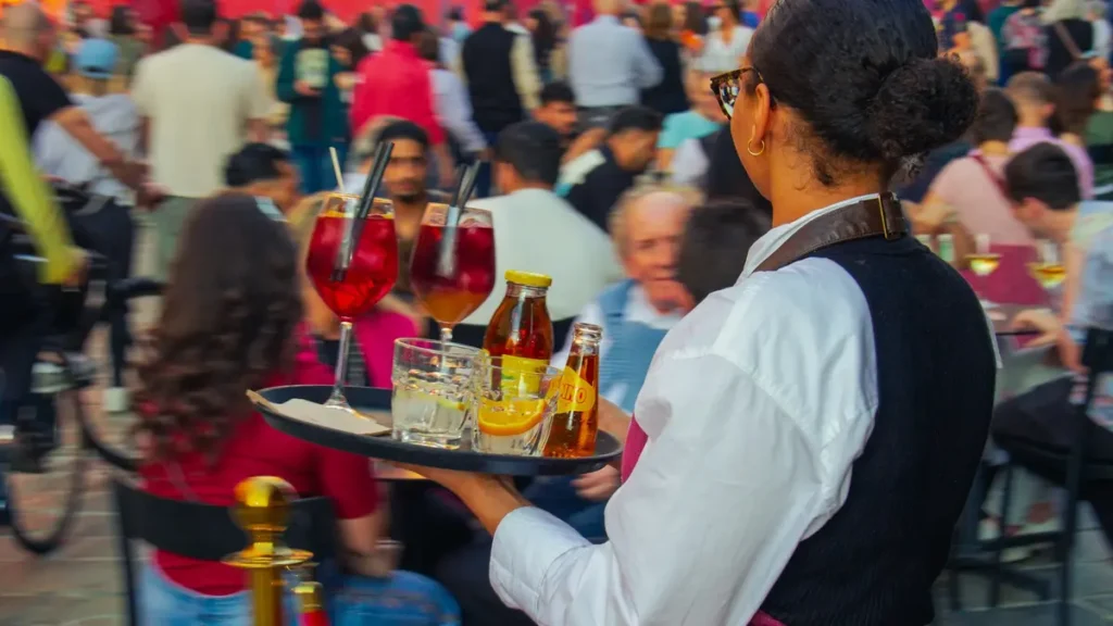 Serveuse portant un plateau de boissons sur une terrasse animée