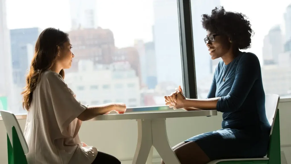 Deux femmes en entretien autour d'une table près d'une fenêtre
