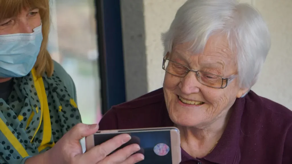 Soignante masquée qui montre un téléphone à une dame âgée souriante