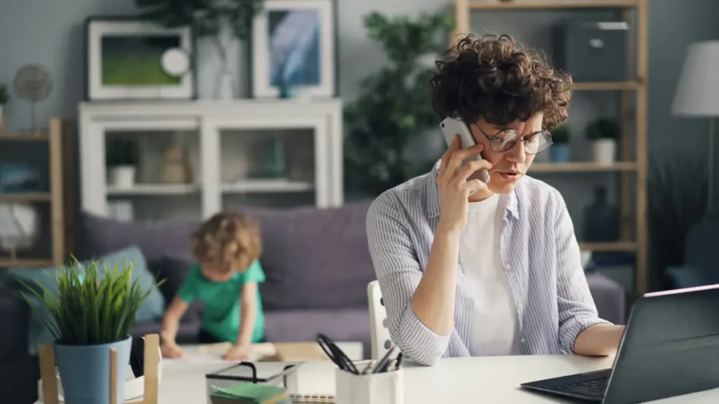 Femme au téléphone devant son ordinateur, son enfant jouant à côté