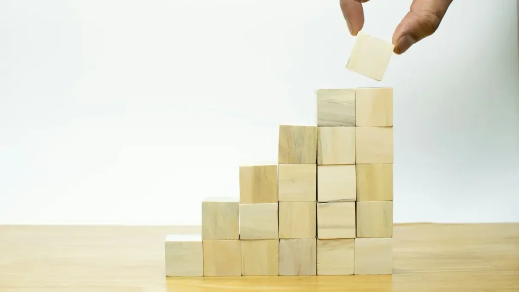 Main qui pose un cube de bois au sommet d'un escalier de cubes