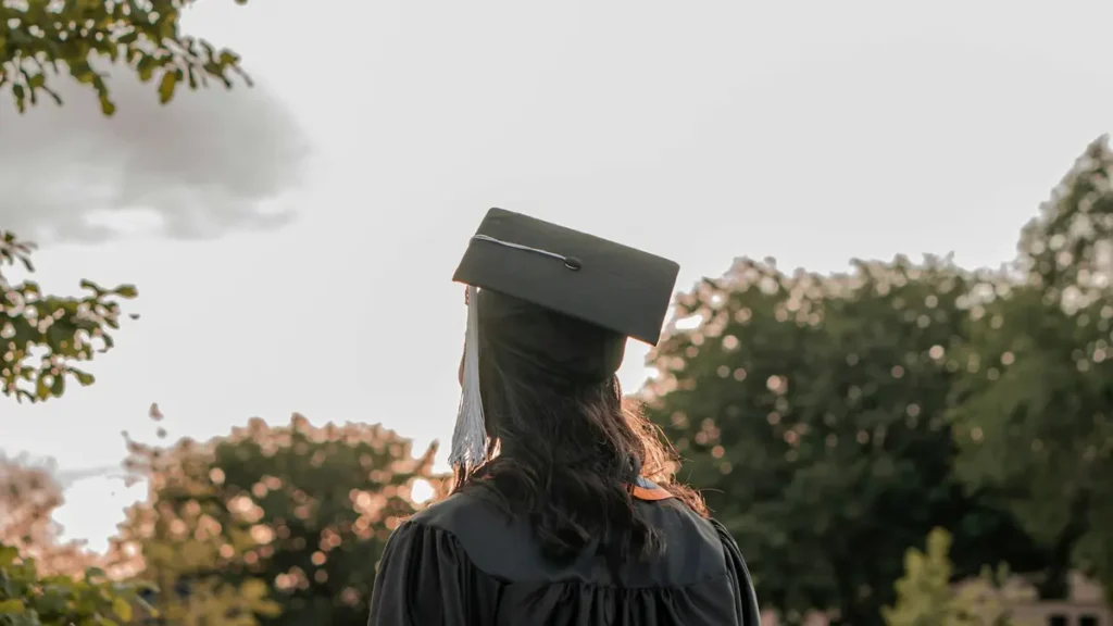Jeune diplômée de dos, portant une toque, face à des arbres