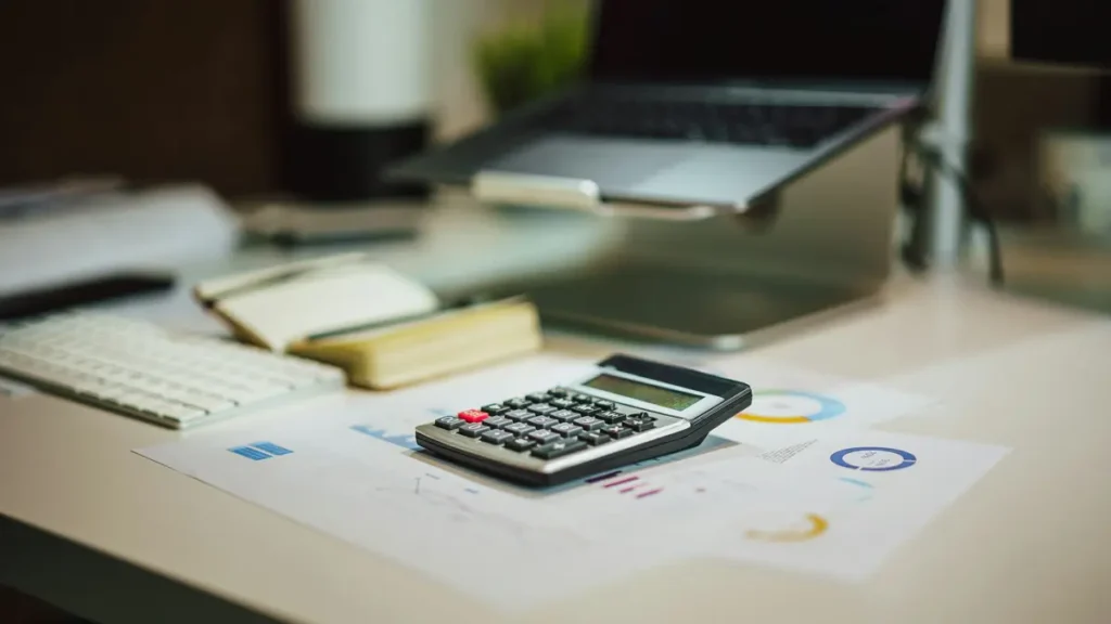 Calculatrice et carnet posés sur un bureau près d'un ordinateur