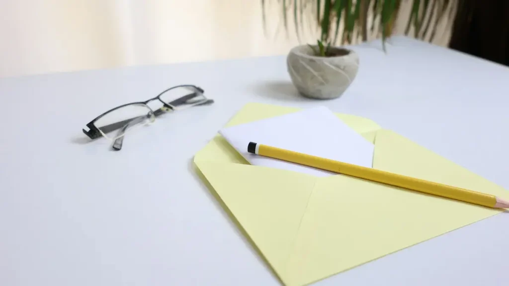 Lunettes, crayon et enveloppe jaune posés sur un bureau