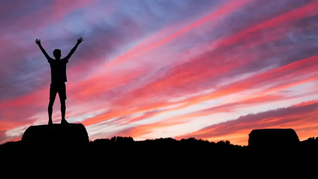 Silhouette d'un homme bras levés au coucher du soleil