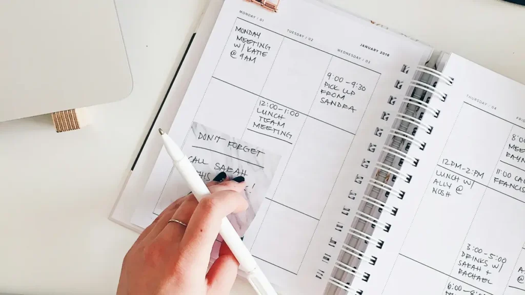 Main qui écrit dans un agenda ouvert sur un bureau