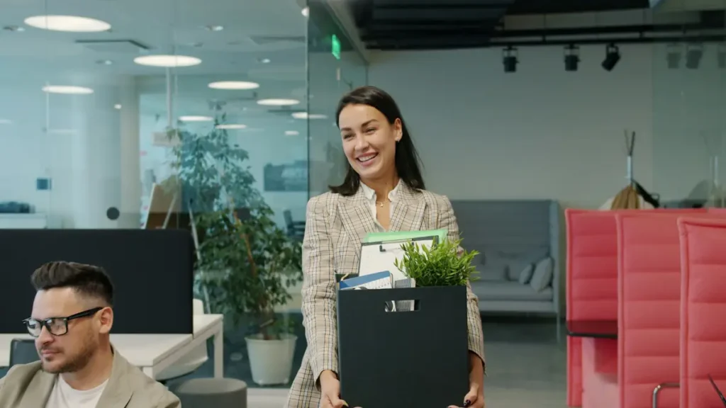 Femme souriante qui quitte un bureau avec un carton