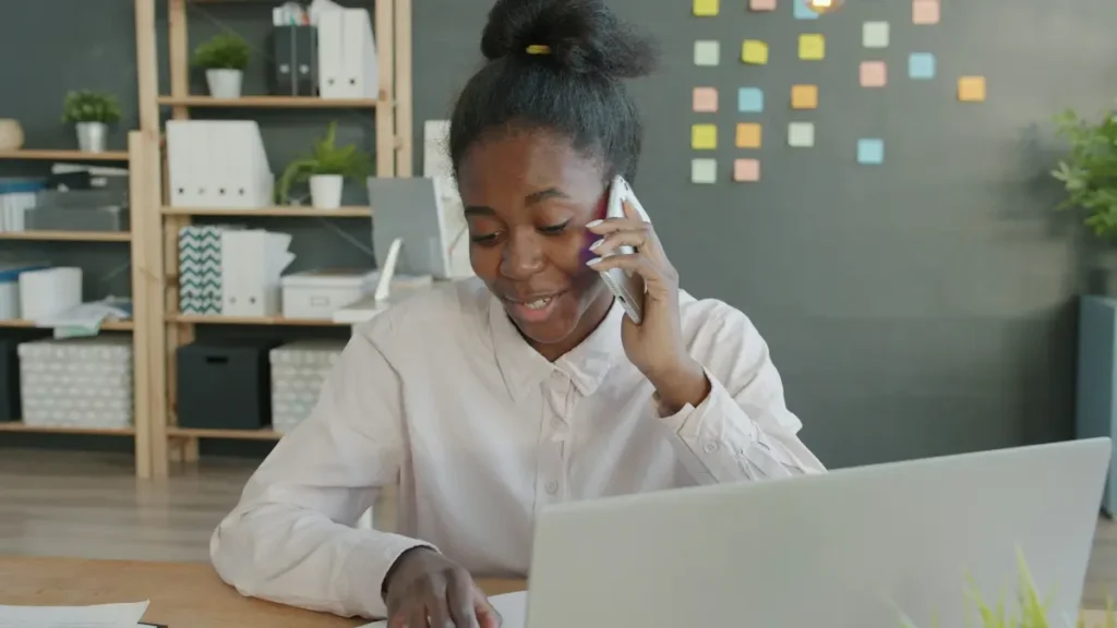 Jeune femme souriante qui téléphone devant son ordinateur