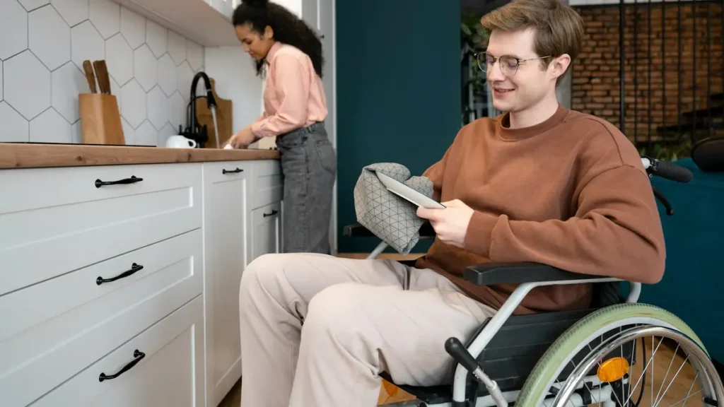 Jeune homme en fauteuil roulant qui consulte une tablette dans une cuisine
