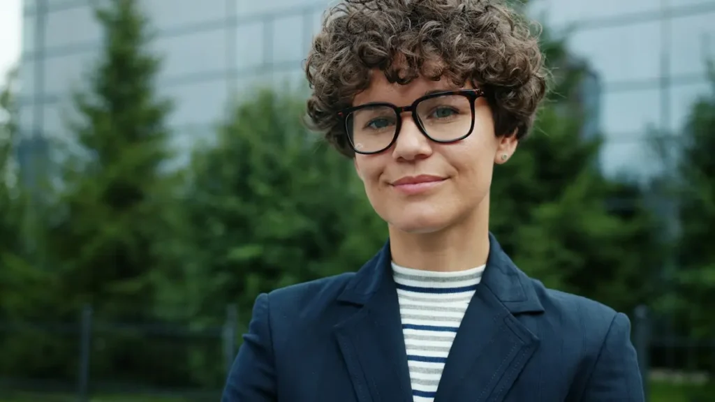 Jeune femme souriante en veste devant un immeuble de bureaux