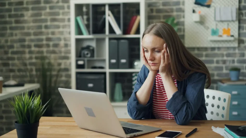 Jeune femme pensive devant un ordinateur portable