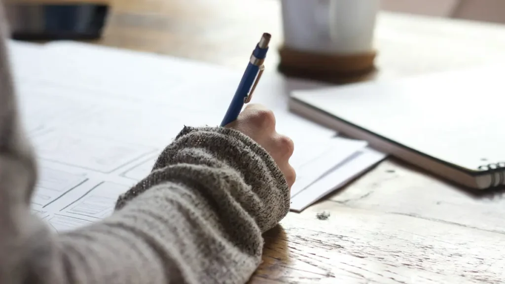 Personne qui écrit à la main sur une table en bois, à côté d'une tasse